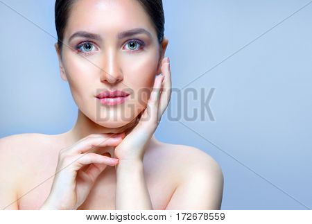 beauty closeup portrait of attractive young caucasian woman brunette on blue background studio shot lips face skin care hands near the face looking at camera spa. Touching her perfect skin. copy spacy