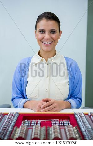 Portrait of smiling optician sitting with trial lens set on table in optical store