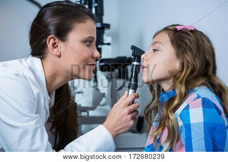 Female optometrist examining young patient with ophthalmoscope in ophthalmology clinic