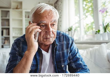 Tensed senior man talking on mobile phone at home