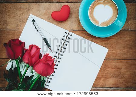 Red roses leather notebook penheart and cup of coffee on wooden background with copy space.Valentines Day background concept Wedding day.Top view vintage tone