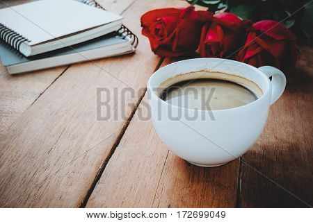 Cup of coffee red rose and notebook on wooden background with copy space.Close up.Valentines Day background concept Wedding day.Top view vintage tone