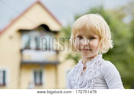 Humeral portrait of little blonde girl outdoor against house.
