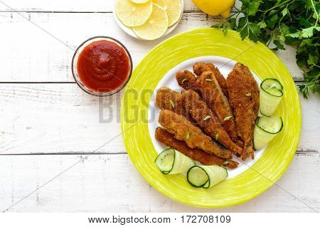 Deep frying small fish capelin on a plate on white wooden background. The top view.