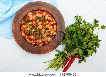 White large beans in sweet and sour tomato sauce in a clay bowl on a light background. Vegetarian cuisine. Lenten meal. The top view