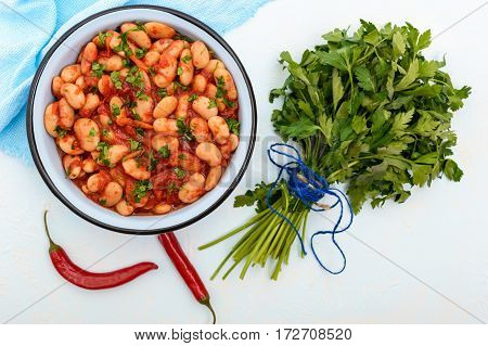 White large beans in sweet and sour tomato sauce in a bowl on a light background. The top view. Vegetarian cuisine. Lenten meal.