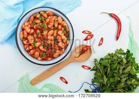 White large beans in sweet and sour tomato sauce in a bowl on a light background. The top view. Vegetarian cuisine. Lenten meal.
