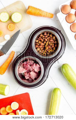 Bowl of dry dogfood with fresh carrot, courgette and meat on white table background top view