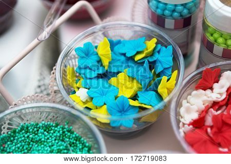 Ice cream treats and toppings sale. Rainbow sprinkles, flowers, non pareil and glitter cupcake decorations, bright yellow and blue. Closeup in plastic plates with spoons. Confectionery store