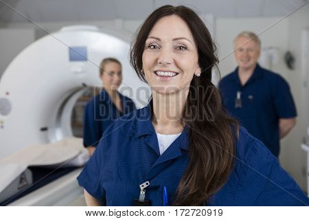 Smiling Female Radiologist With Colleagues Standing By MRI Machi