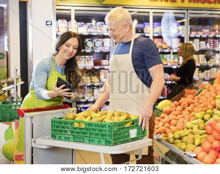 Worker Showing Digital Tablet To Colleague Working In Fruits Dep