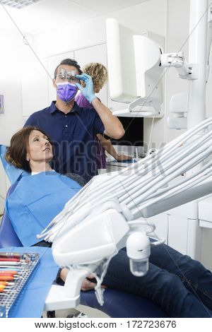 Male Dentist Examining Patient While Assistant Working At Dentis