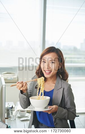 Portrait of pretty Vietnamese business woman eating noddles with chopsticks