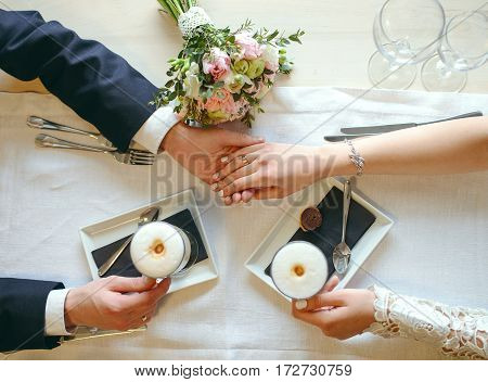 Close-up shot of hands. Groom holds bride's hand at the table at cafe. Top view