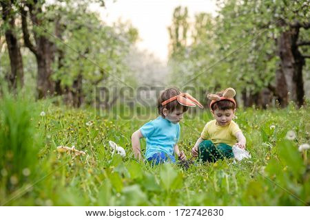 Two Little Kids Boys And Friends In Easter Bunny Ears During Traditional Egg Hunt In Spring Garden,