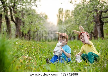 Two Little Kids Boys And Friends In Easter Bunny Ears During Traditional Egg Hunt In Spring Garden,