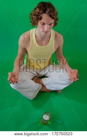Peaceful young man doing yoga and meditation with mug of beer