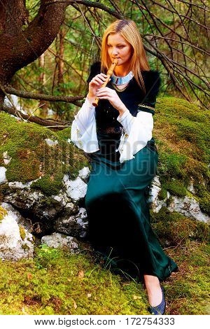 beautiful girl in a historical costume playing her flute in forest. and light graphic effect