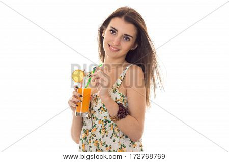 young beautiful brunette girl in sarafan with floral pattern drinks orange cocktail and smiling on camera isolated on white