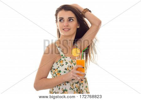 young beautiful brunette girl in sarafan with floral pattern drinks orange cocktail and looks aside isolated on white