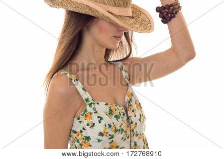 young cute brunette girl in sarafan with floral pattern and straw hat with wide brim posing with hide eyes isolated on white