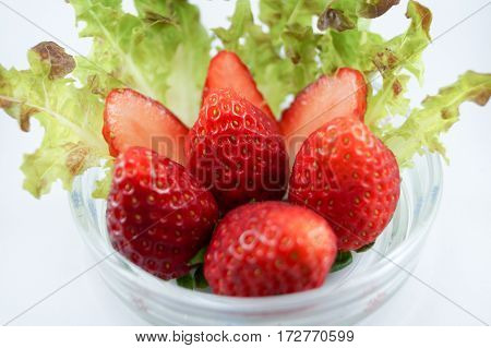 Strawberries put in glass dish with vegetables and strawberries cut into pieces.