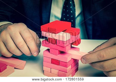 Businessman builds big tower with jenga bricks - planning risk and strategy in business - retro style
