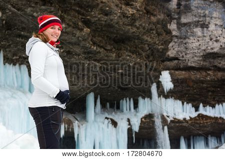 Young pregnant woman smiling on winter landscape. Icicles and snow in the background.