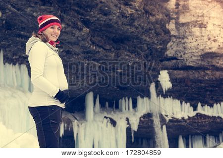 Young pregnant woman smiling on winter landscape. Icicles and snow in the background.