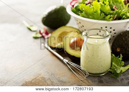 Avocado ranch dressing in small jar with salad leaves in a collander with copy space