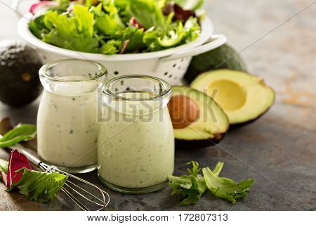 Avocado ranch dressing in small jar with salad leaves in a collander