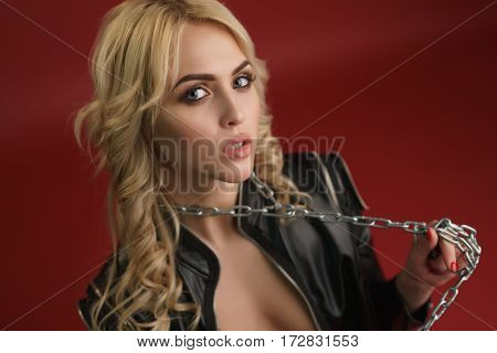 Gorgeous sexy longhaired blonde in black leather jacket and thick metal chain over her neck on red background