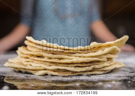 Stack of Homemade Tortillas on floured surface with Woman in Background