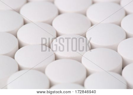 Round white pills closeup sit on a table.