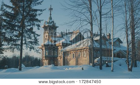 Beautiful traditional snow-covered russian cottage - terem surrounded by a forest and evergreen fir tree near it.