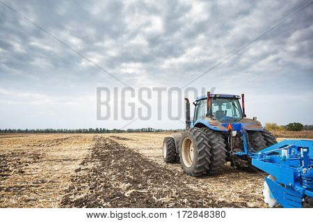 Farmer riding a tractor, a tractor working in a field, agricultural machinery in the work, tractor in the background cloudy sky