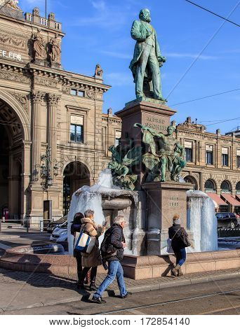 Zurich, Switzerland - 27 January, 2017: people photographing frozen fountain at the basement of the monument to Alfred Escher, Zurich main railway station building in the background. Temperatures in Zurich during January 2017 were unusually low.