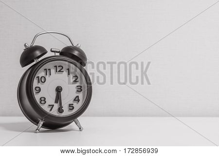 Closeup alarm clock for decorate show half past six or 6:30 a.m.on white wood desk and cream wallpaper textured background in black and white tone with copy space