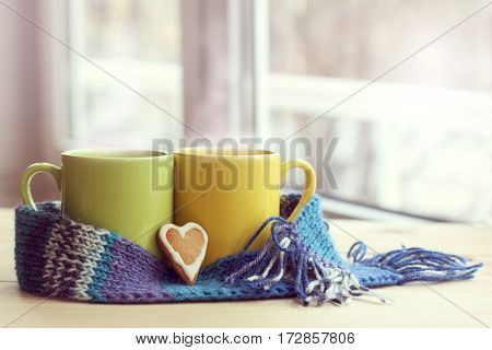 two mugs tied a warming scarf on a table against the window / together warmer spring