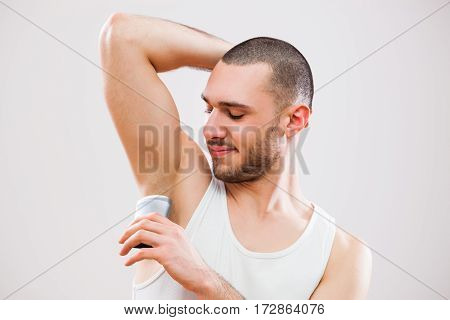 Young man is applying antiperspirant to his armpit.