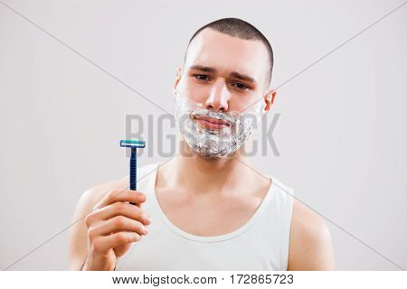 Young man is bored because he has to shave his beard.