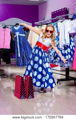 Little fashion-monger girl wearing beautiful pin-up dress and sunglasses goes shopping. Children's fashion. Sale and shopping concept. 