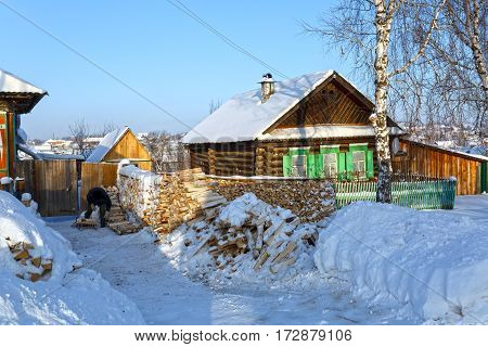 Snow-covered wooden houses and heaps of firewood in a russian old believer village Visim. Ural region, Russia.