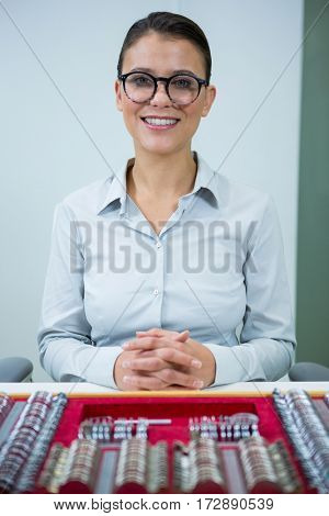 Portrait of smiling optician sitting with tool box on table in optical store