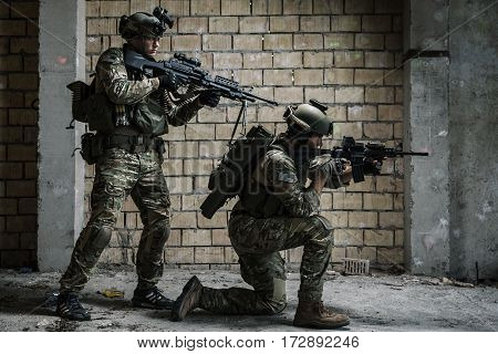 Pair of US Army Rangers with machinegun and rifle moving along the wall after each other on military mission