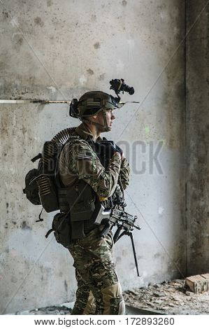 US Army Ranger with machinegun and night vision goggles standing near the wall. Side view profile