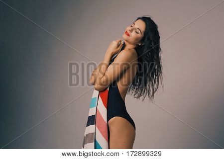 Fashion photo of beautiful and young lady in swimsuits posing in studio, holding colorful towel