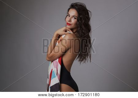 Fashion photo of beautiful and young lady in swimsuits posing in studio, holding colorful towel