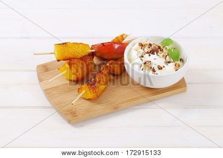 pear and orange skewers with bowl of yogurt, chopped nuts and almonds on wooden cutting board