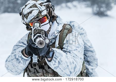 Winter arctic mountains warfare. Action in cold conditions. Trooper with weapons in forest somewhere above the Arctic Circle, pointing at camera